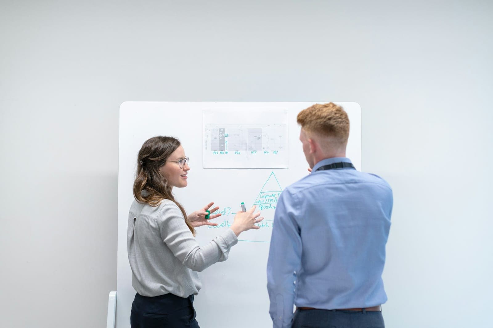 Duas pessoas conversam diante de um quadro branco com um gráfico impresso e anotações à mão