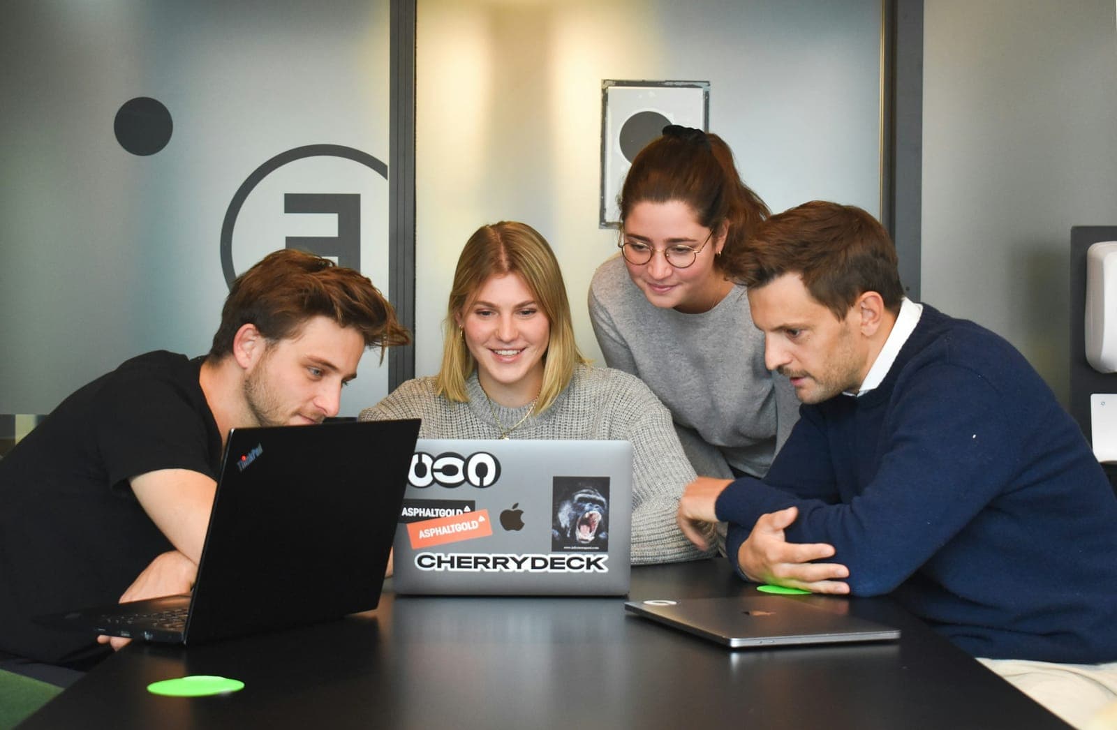 Quatro colegas reunidos em volta de um notebook numa mesa de escritório, olhando juntos para a tela