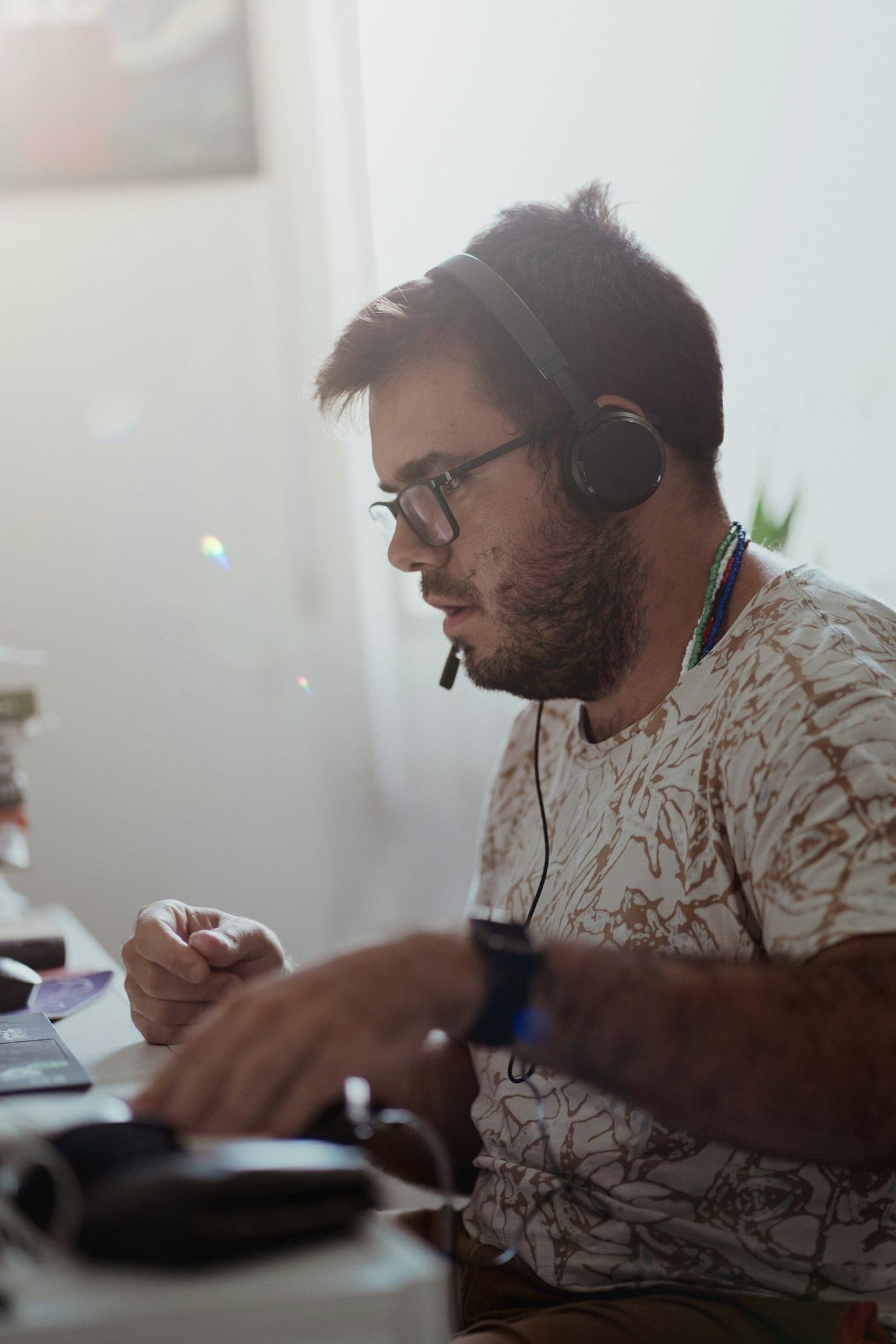 Homem de óculos com fone e microfone de headset conversa enquanto usa o computador numa mesa
