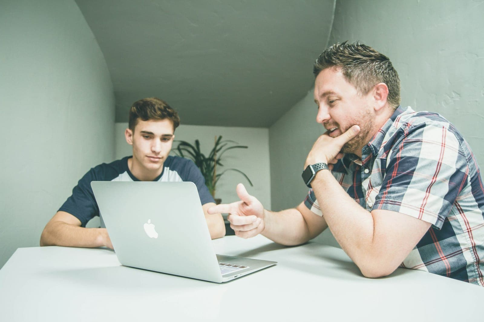 Homem aponta para a tela de um notebook enquanto explica algo a um colega sentado ao lado